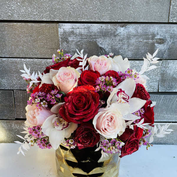 Bouquet of red and blush roses with white orchids in a gold mask vase