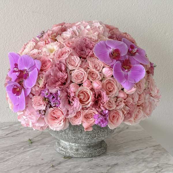 Pink rose and orchid arrangement in a stone pedestal vase