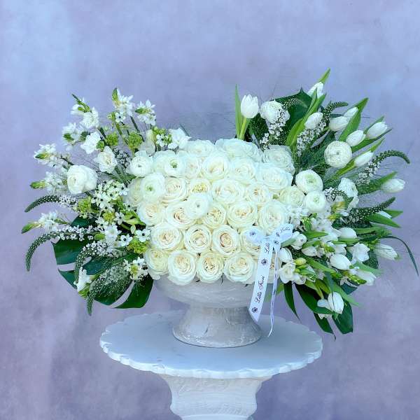 Large white rose arrangement in a white pedestal vase