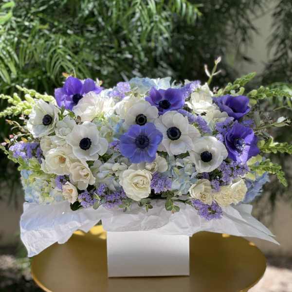 White and purple floral arrangement in a white box