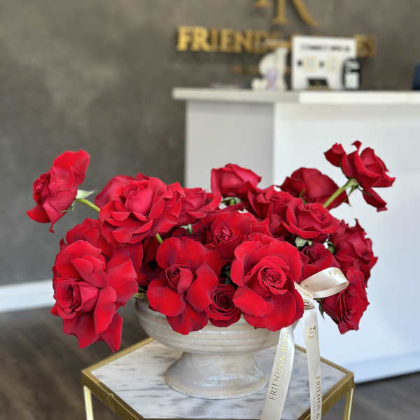 Red roses arranged in a white pedestal vase with a ribbon