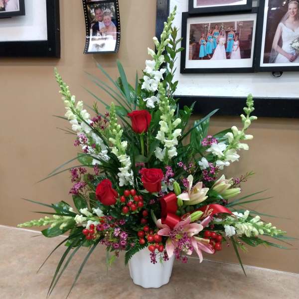 Tall floral arrangement with red roses, white snapdragons, pink lilies, and a white vase