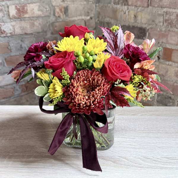 Bouquet of red roses and yellow chrysanthemums in a glass vase with a burgundy ribbon