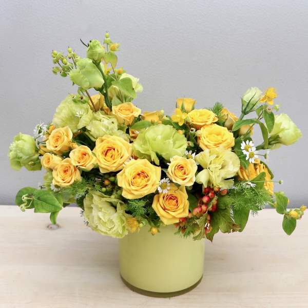 Yellow roses and green blooms arranged in a pale vase
