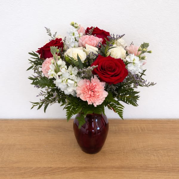 Bouquet of red and white roses with pink carnations in a burgundy vase