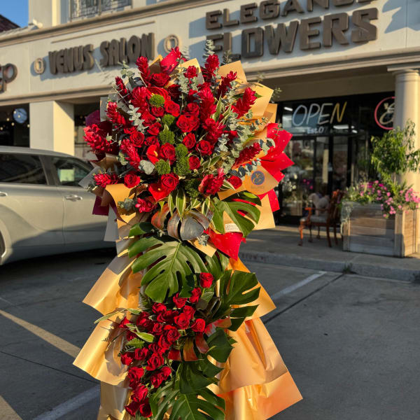 Tall bouquet of red roses and tropical leaves wrapped in gold paper