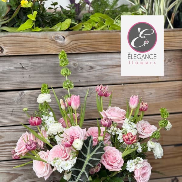 Pink and white flower arrangement in a wooden container on a small pedestal stand