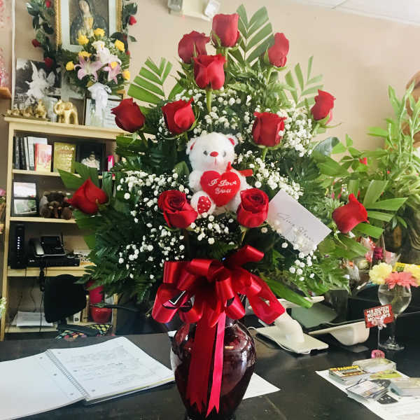 Red roses arranged in a vase with a teddy bear and heart decoration