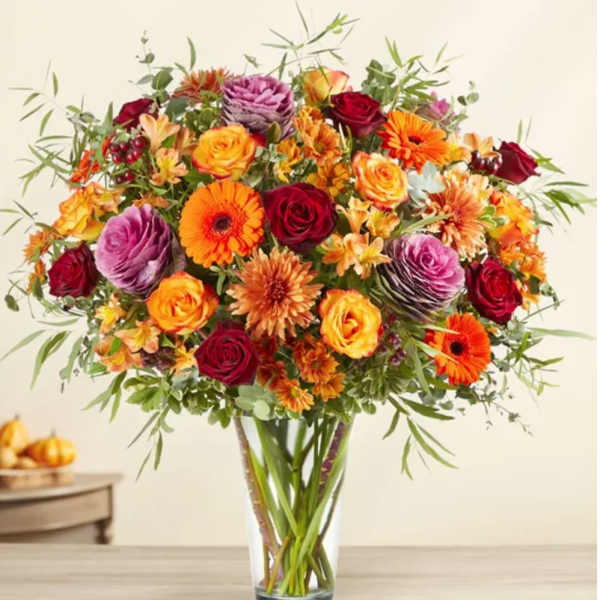 Mixed bouquet of roses, gerbera daisies, and orange blooms in a clear vase