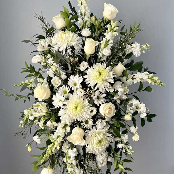 Tall standing spray of white roses, daisies, and snapdragons on a metal easel.