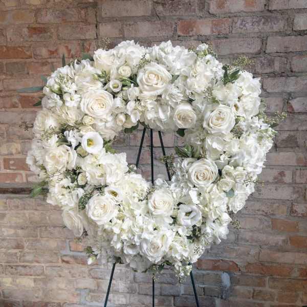 Heart-shaped wreath of white roses and hydrangeas on a metal stand