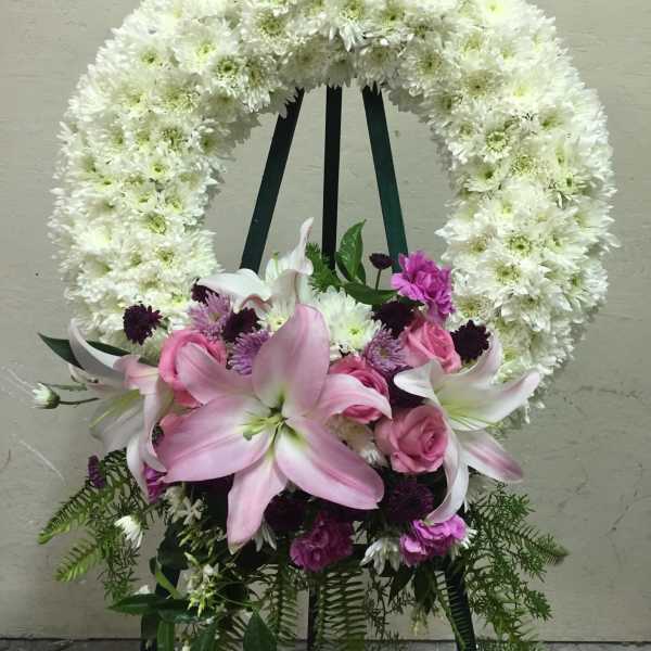 White floral wreath on an easel with pink lilies and roses at the base