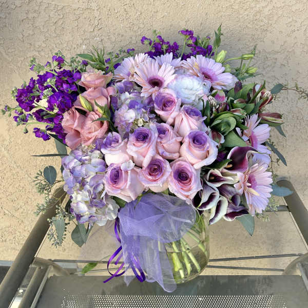 Bouquet of pink and purple flowers in a glass vase with a lavender ribbon