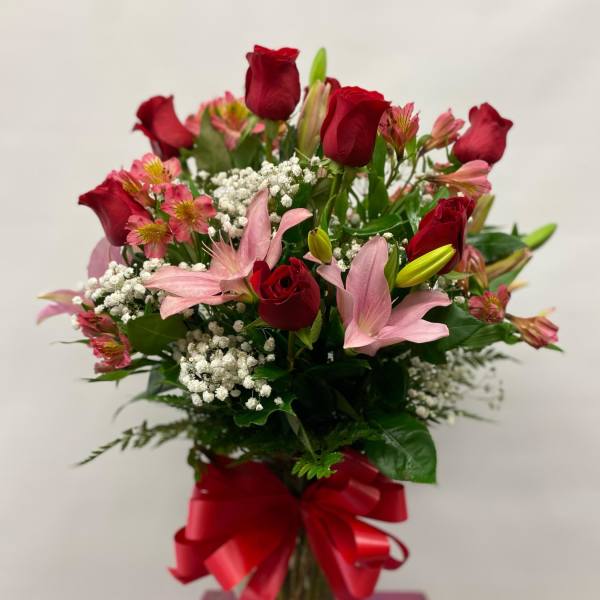 Bouquet of red roses and pink lilies in a glass vase with a red ribbon