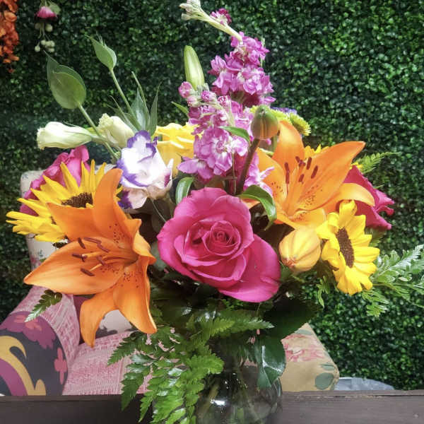 Mixed bouquet of pink roses, orange lilies, and sunflowers in a glass vase