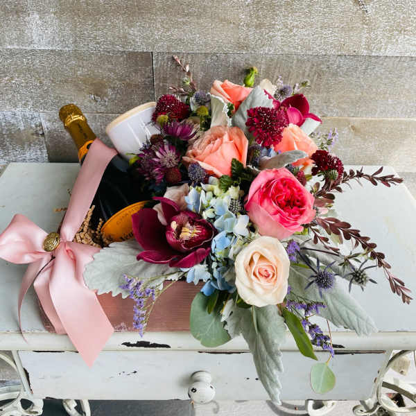 Bouquet of roses, orchids, and hydrangeas with a champagne bottle and candle
