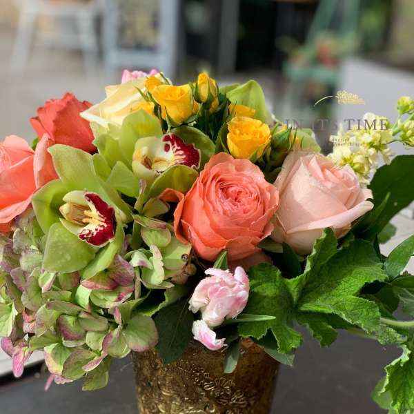 Mixed bouquet of roses, orchids, and hydrangeas in a gold vase