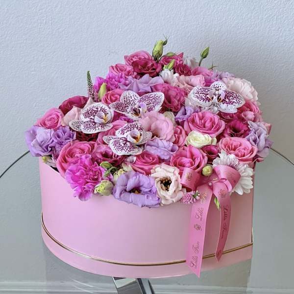 Pink and lavender floral arrangement in a round pink box with ribbon