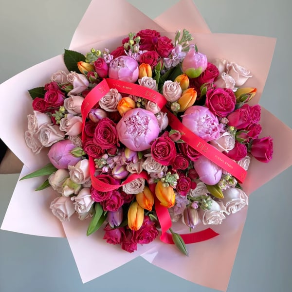 Large bouquet of pink roses, peonies, and tulips wrapped in pale pink paper