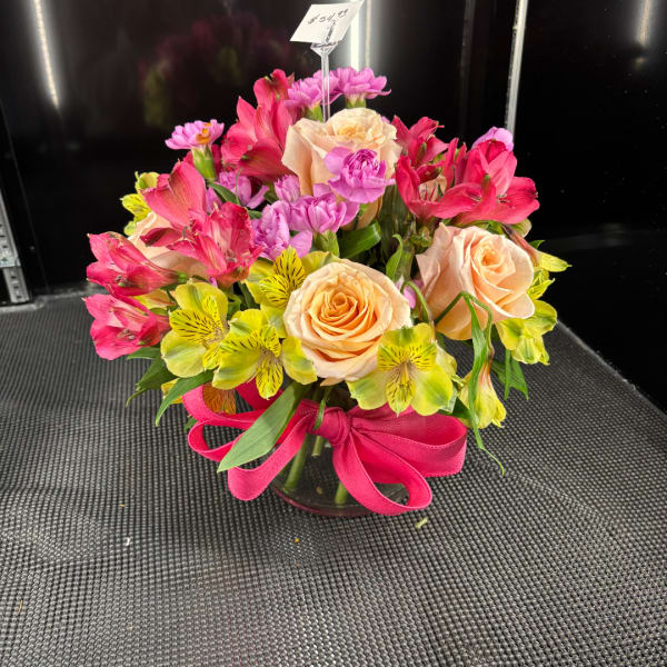 Mixed bouquet of peach roses, pink flowers, and yellow alstroemeria in a glass vase