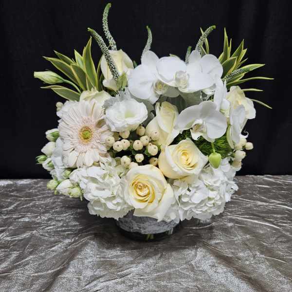 White floral arrangement with roses, orchids, and a gerbera daisy in a low vase