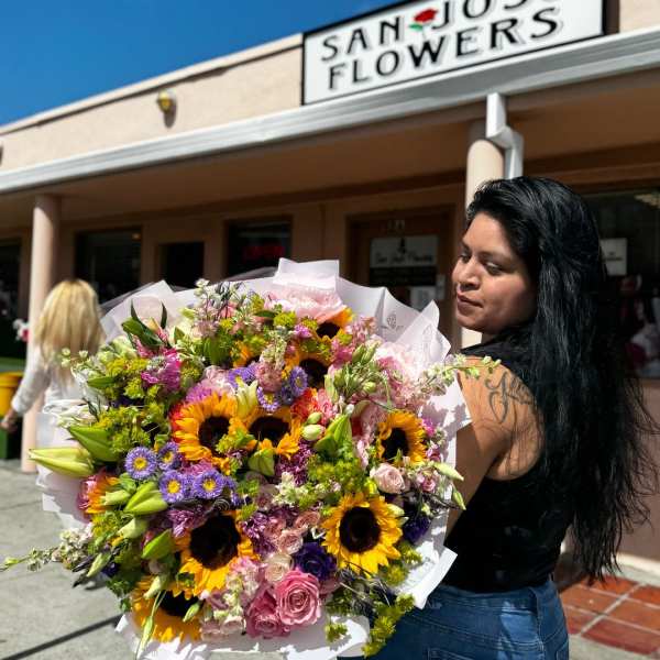 Large mixed bouquet with sunflowers, roses, and lilies wrapped in white paper