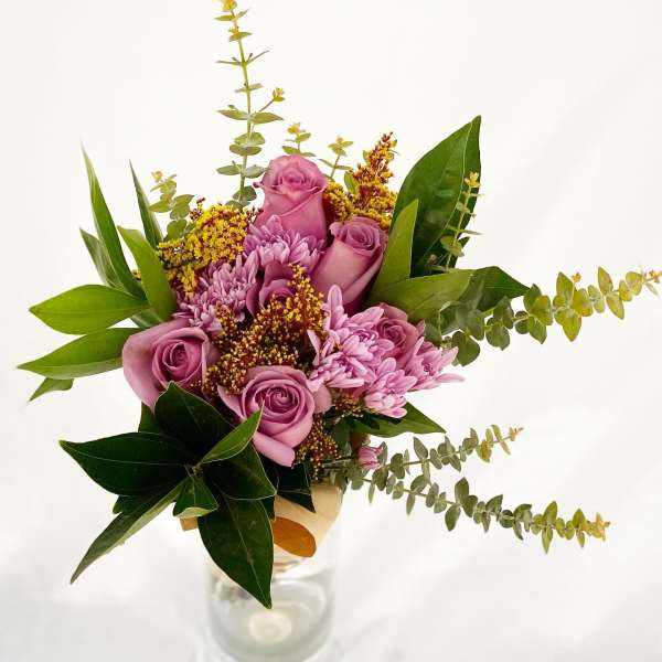 Tall bouquet of mauve roses and lavender mums with yellow filler in a clear glass vase