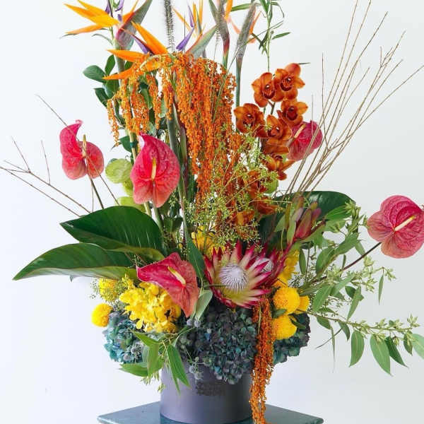 Tall tropical floral arrangement with orange birds of paradise and pink anthuriums in a vase