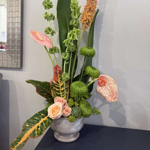 Tall tropical floral arrangement with pink anthuriums and green chrysanthemums in a gray vase