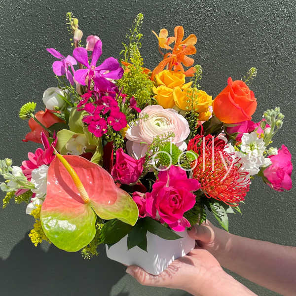 Bright mixed arrangement of pink, yellow, and orange flowers in a white cube vase.