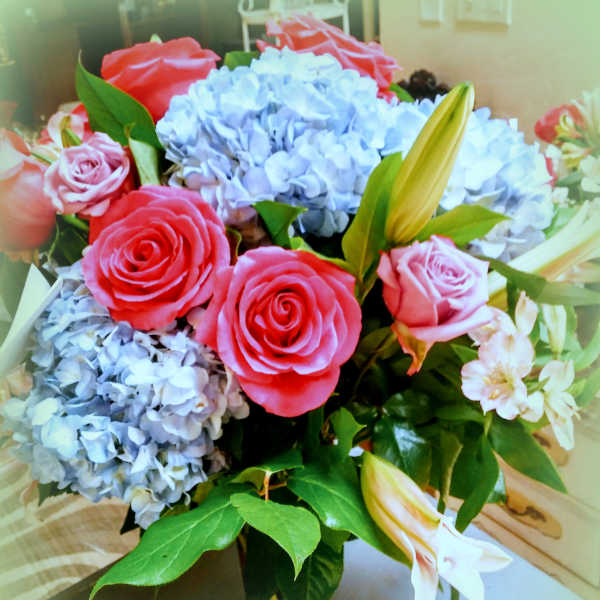 Bouquet of pink roses, blue hydrangeas, and white lilies in a glass vase