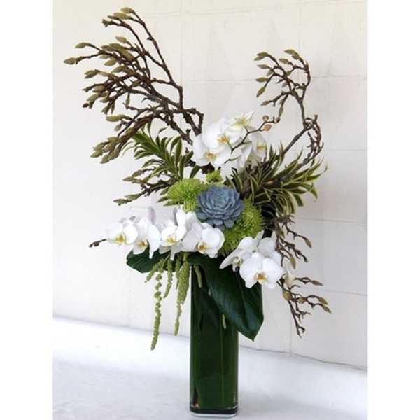 Tall floral arrangement with white orchids, blue succulents, and green accents in a glass vase
