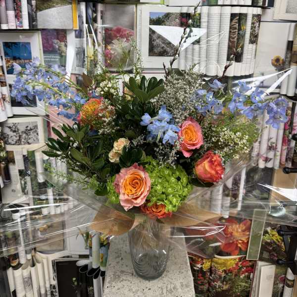 Mixed bouquet of orange and pink roses with blue flowers in a glass vase