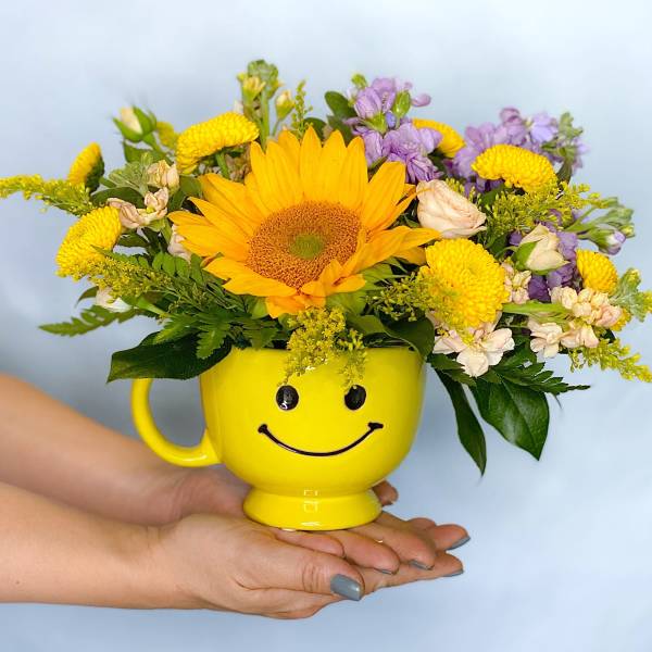 Yellow mug with a smiley face holding a mixed flower arrangement
