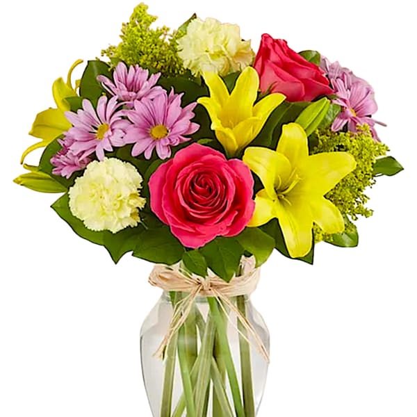 Mixed bouquet of pink roses, yellow lilies, and daisies in a glass vase