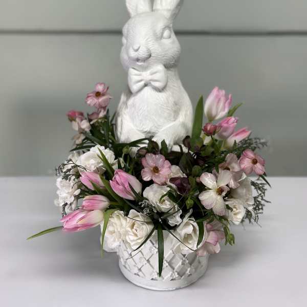 White bunny figurine in a flower basket with pink and white tulips