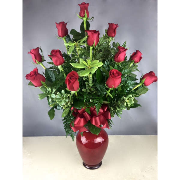 Red roses arranged in a red vase with a ribbon bow