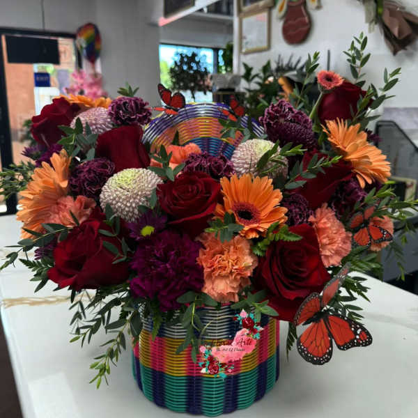 Colorful mixed flower arrangement in a rainbow basket with butterfly picks