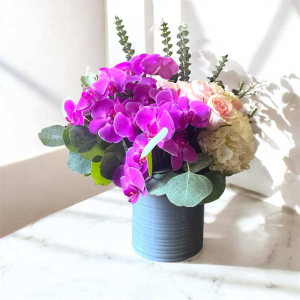 Purple orchids and pale roses arranged in a dark vase