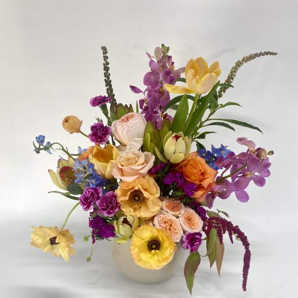 Colorful mixed bouquet in a white vase with orchids and roses