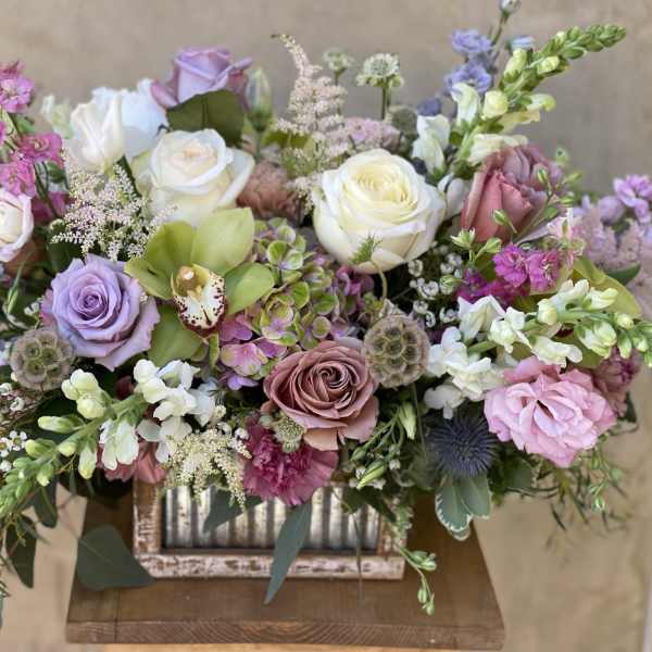 Mixed pastel bouquet with roses, orchids, and snapdragons in a rustic container