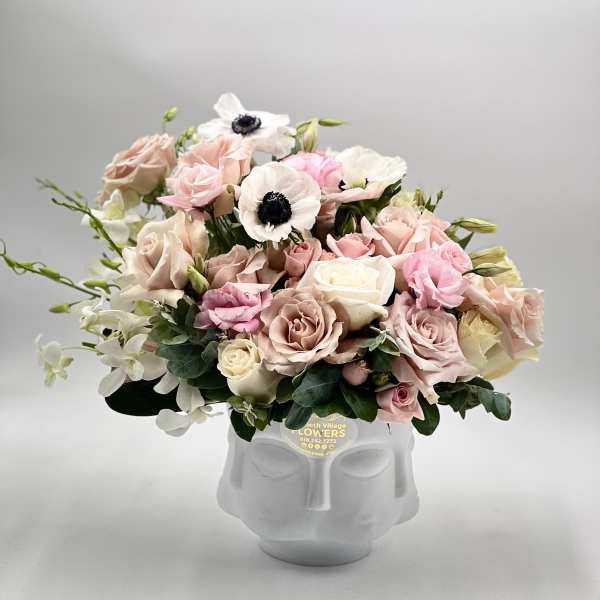 Low pastel arrangement of roses, anemones, and orchids in a white ceramic face vase