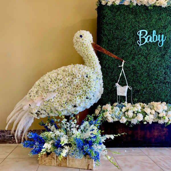 White floral swan display beside a green backdrop with blue flowers
