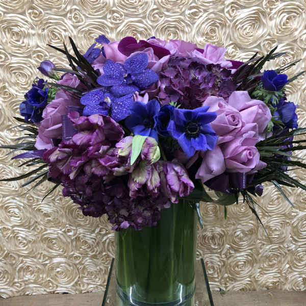 Purple and blue floral arrangement in a tall glass vase