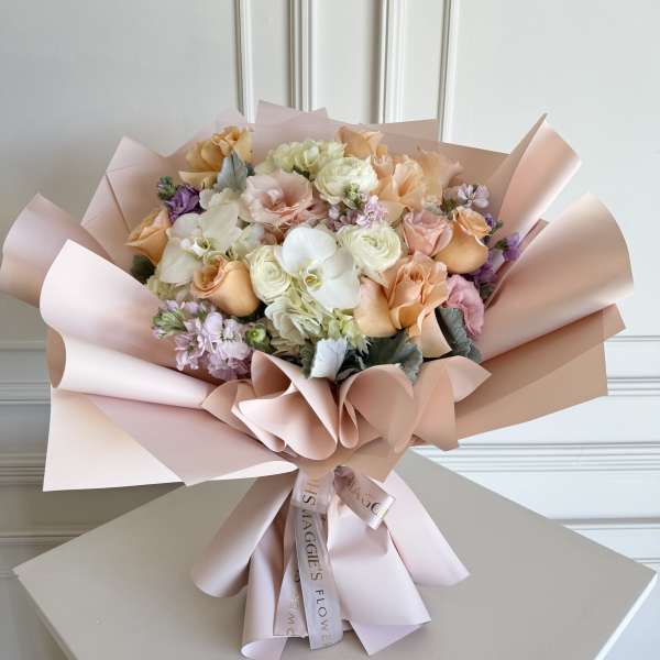 Bouquet of peach, pink, and white flowers wrapped in blush paper