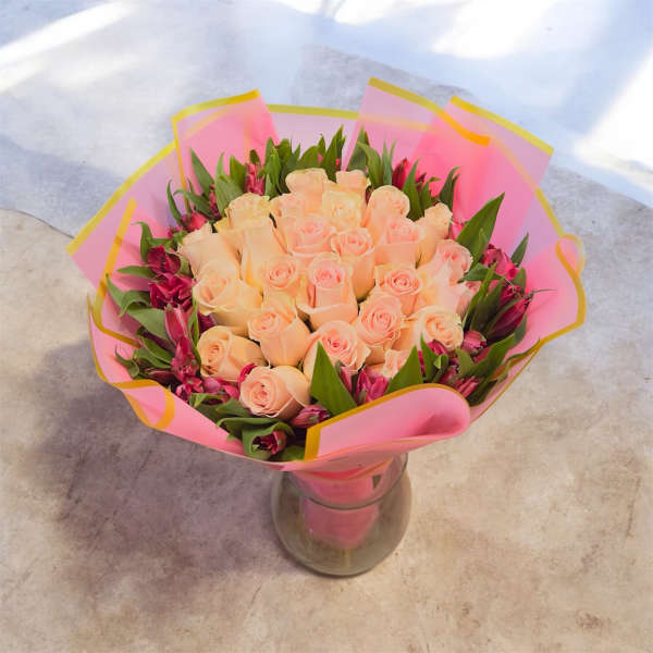 Peach roses in a glass vase with pink wrap