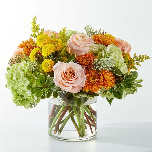 Bouquet of peach roses, yellow mums, and green hydrangeas in a glass vase