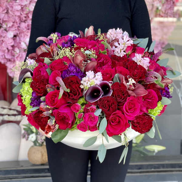 Large bouquet of red and pink roses with purple accents in a white container