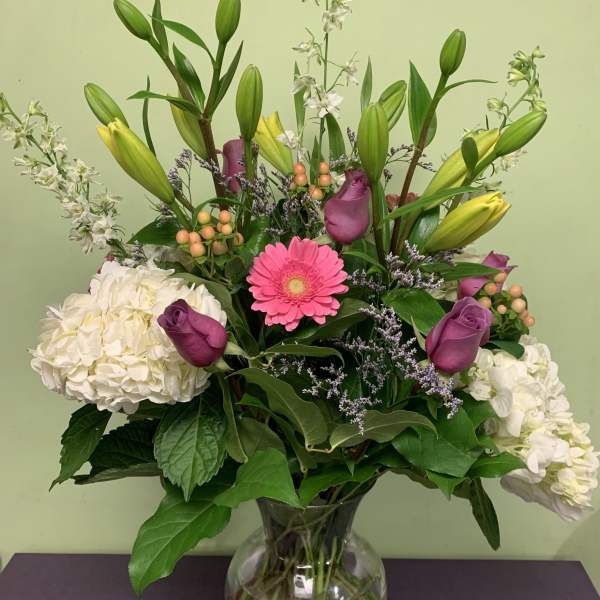 Mixed bouquet with lilies, roses, hydrangeas, and a pink gerbera in a glass vase