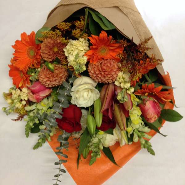 Mixed bouquet with orange daisies, roses, and lilies wrapped in brown paper